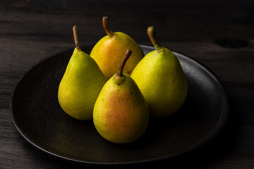 top view of four green pears in black plate on dark table, horizontal