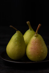 Fototapeta na wymiar Close-up of green pears with water drops on black plate, black background, vertical, with copy space