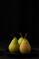 Top view of green pears with water drops on black plate, black background, vertical, with copy space