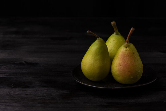 View of green pears with water drops in black plate on dark wooden table, horizontal, with copy space