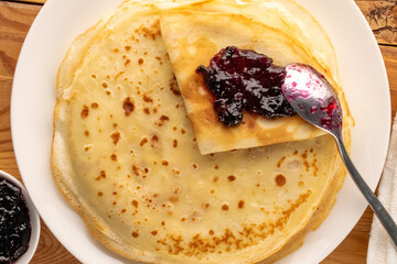Several sweet pancakes with ceramic plate and jam on wooden table, macro, top view.