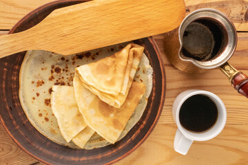 Several sweet pancakes with ceramic plate, cup of coffee and wooden spatula on wooden table, macro, top view.