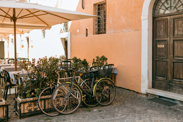 Bicycles parked on the street. Old bike against the orange wall at home. City transport concept. Lush green plants growing in pots near door of house. Cozy old street in Trastevere in Rome, Italy.