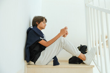 Teenage boy sitting on stairs and using smartphone. Teenager browse social media, communicate with...