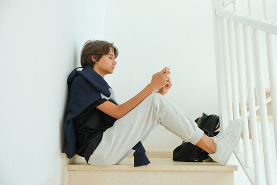 Teenage boy sitting on stairs and using smartphone. Teenager browse social media, communicate with friends, family, play games, watch videos, use apps for entertainment