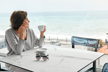 Freelance business woman enjoying a fragrant coffee alone in cafe in the morning near panoramic...