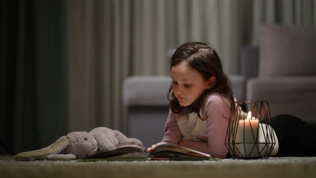 The girl reads a book lying on the carpet at home