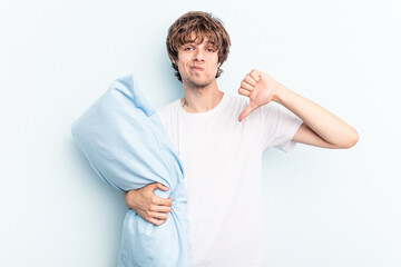 Young caucasian man going to sleep holding a pillow isolated on blue background showing a dislike...