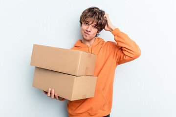 Young man making a move while picking up a box full of things isolated on blue background being shocked, she has remembered important meeting.