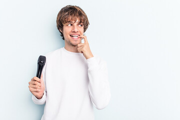 Young caucasian singer man isolated on blue background relaxed thinking about something looking at a copy space.