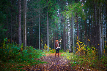 Girl in a leather jacket, a big red fox fur hat and with a crossbow in the forest in autumn. A...