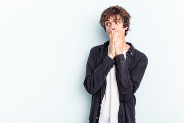 Young caucasian man isolated on blue background thoughtful looking to a copy space covering mouth with hand.