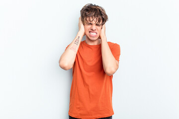 Young caucasian man isolated on blue background covering ears with hands.