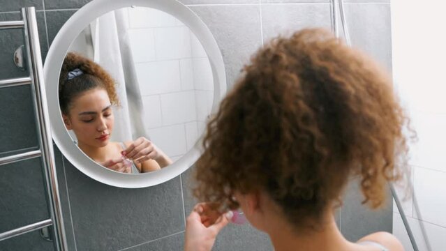 beautiful serious woman looking at mirror, applying eye patches in bathroom, slow motion. Spending quality time, lifestyle, domestic life gitl reflects in mirror wellness health face care back view