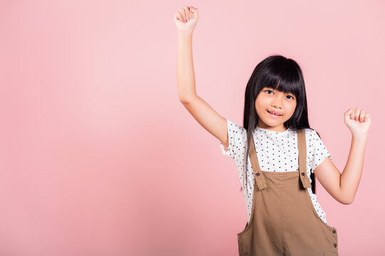 Yes. Asian little kid 10 years old celebrating great success with arms raised at studio shot isolated on pink background, Happy and excited child girl positive smiling cheerful