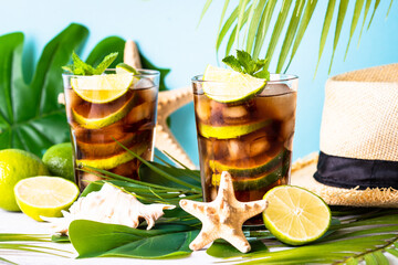 Cuba Libre alcoholic cocktail, iced drink with palm leaves and sea shells. Tropical vacation.