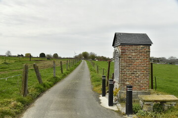 Chemin asphalt&eacute; entre les champs et p&acirc;turages sous un ciel gris &agrave; Ghislenghien (Ath) 