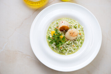 White plate with green pea risotto and seared scallops, elevated view on a beige marble background, horizontal shot