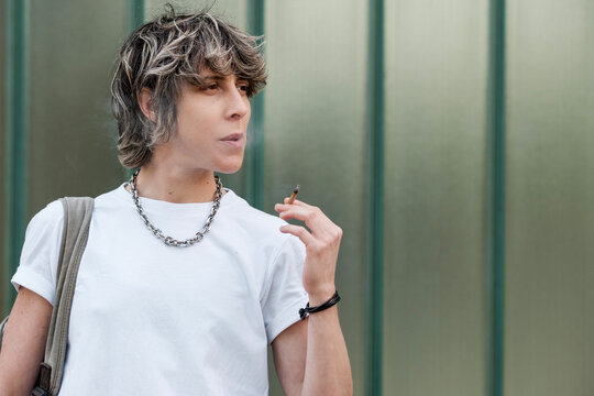 Androgynous non-binary person is smoking outdoors.