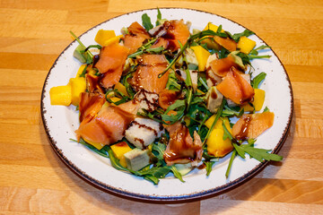 Fresh healthy salad with mango, avocado, salmon, arugula and croutons on wooden table