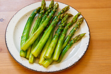 Green boiled asparagus in a plate on a wooden table