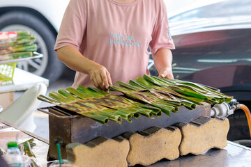 Merchant Grill Khanom jak - Thai style sweetmeat made from flour, coconut and sugar, grilled and wrapped with nipa palm leaves © patipak