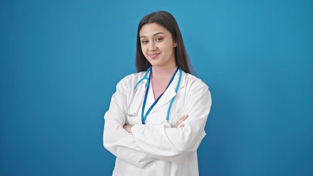 Young beautiful hispanic woman doctor smiling confident standing with arms crossed gesture over isolated blue background