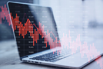 Close up of laptop on desktop with falling red business graph grid on blurry background. Crisis, recession and stock market concept. Double exposure.