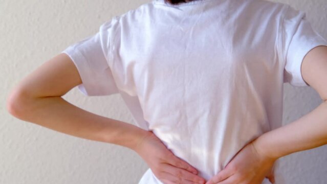 back of boy, child 8-10 years old in white t-shirt grabbed sore spot, curved spine, wrong posture, symbol of pain in spine, concept of osteochondrosis, scoliosis, back pain, intervertebral hernia
