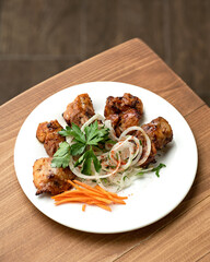Meat skewers with onions, carrots on white plate. Pieces of fried meat with vegetables garnished with parsley. Azerbaijani, Middle Eastern cuisine. Wooden background. Top view. Copy space.