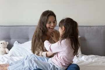Joyful young mother tickling little preschool kid girl, playing active games with daughter on bed, having fun, laughing, smiling, enjoying family weekend, leisure time, motherhood