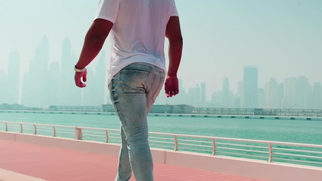 A young man in jeans, sneakers and a white T-shirt walks along the parapet along the embankment