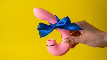 Woman holding curved pink vibrator with blue ribbon on yellow background. Copy space. 