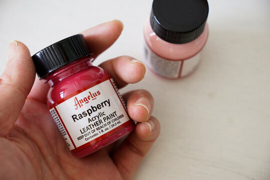 Cropped hand holding a bottle of Angelus raspberry leather paint in Ho Chi Minh City, Vietnam on September 19, 2022                            