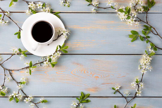 Cup of fresh black coffee and cherry blossom branches on blue wooden background. Coffee break. Spring flowers. Flat lay, top view.