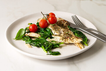 plate with sea bass fillet with spinach and tomatoes on a light table	
