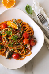 white bowl with pasta with sea bass and tomatoes on a light marble table
