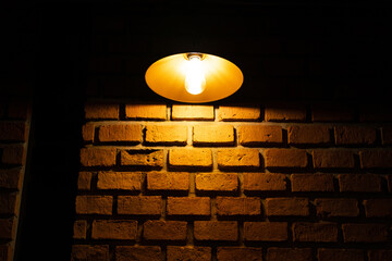 A classic design lamp with lighting is glowing in warm light shade on brick wall. Photo contain...