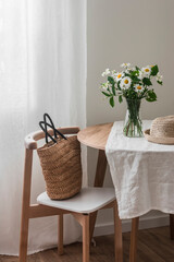 The summer mood in the living room is a bouquet of daisies, a hat on a round table and a straw bag on a Scandinavian-style chair