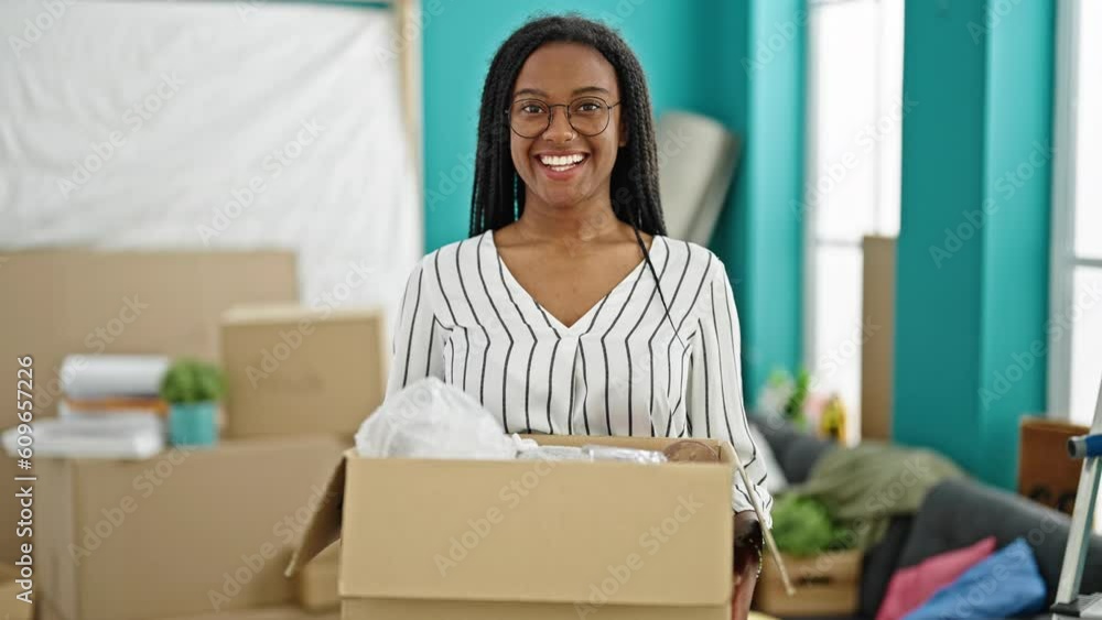 Wall mural African american woman smiling confident holding package at new home