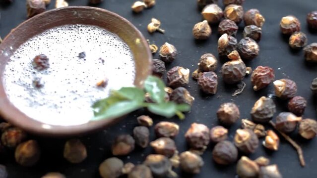 Sapindus mukorossi or soapnuts or areetha on a black-colored surface along with its fermented water used for hair care and cosmetics.
