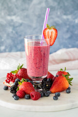 A mixed berry smoothie surrounded by fresh berries, ready for drinking.