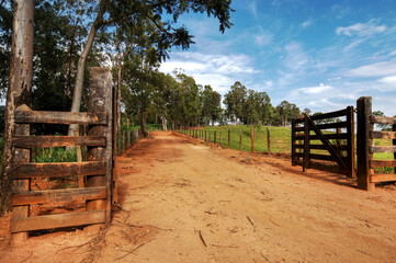 Estrada rural de terra com porteira aberta para a fazenda 