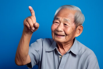 Asian grandfather looking and smiling with rised index finger on blue background. Neural network generated in May 2023. Not based on any actual person, scene or pattern. Generative AI