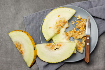 Melon slices with seeds and a knife on a gray plate. Gray napkin.