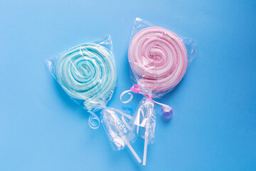 Candy on a stick. Spiral sweets. Candies of two colors pink and blue on a blue background. Candies in plastic packaging.