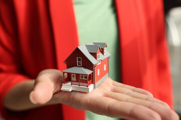 Woman realtor in jacket holds small house model on palm