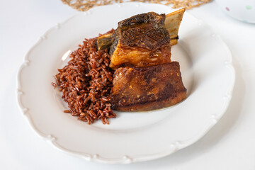 Baked beef rib with red rice on white plate.