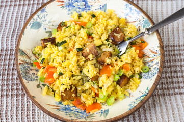 Turmeric rice with green onion, orange pepper and tempeh on decorative plate, fork.