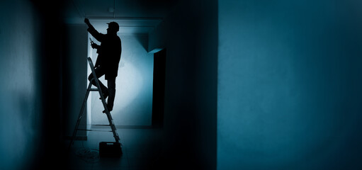 Man electrician. Worker in dark corridor. Silhouette repairman standing on ladder. Repair lighting...